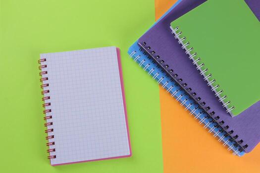 Many multi-colored notebooks and a notebook on a bright multi-colored background. school supplies. Top view photo