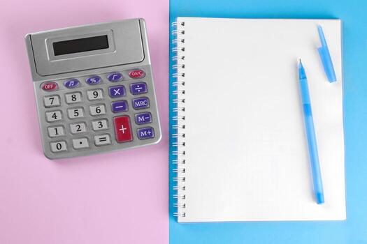 Calculator and notebook with pen on a blue and pink background. view from above. stationery photo