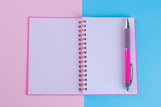 Pink notebook in unfolded form with a pink handle on a bright multi-colored background. School supplies photo
