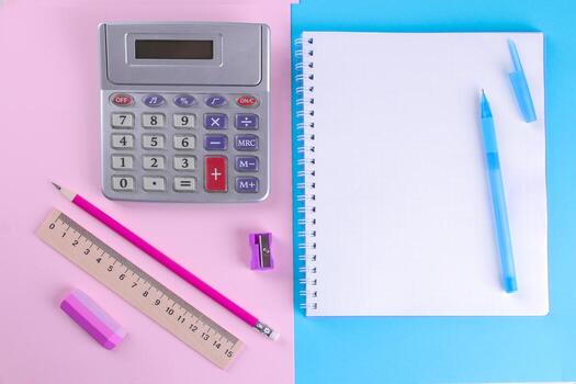 Notebooks and a calculator with different stationery on a bright orange and green background. School supplies. Top view photo