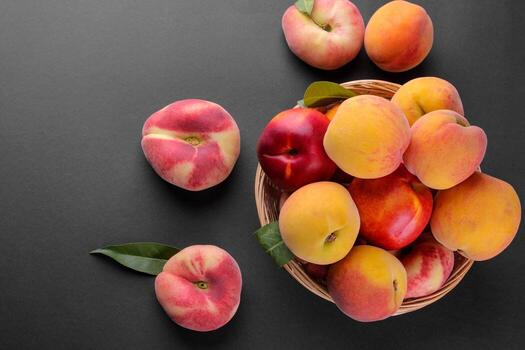 Many different varieties of peaches in a wicker basket on a black background. Top view photo