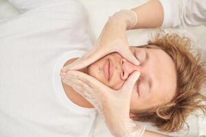 facial masaje terapia para relajación en caucásico masculino adulto con enguantado manos en rostro. foto