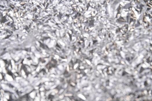 Crumpled silver foil texture with shiny metallic surface and irregular patterns in soft focus. photo