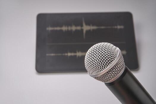 Close up of microphone in front of tablet displaying audio waveforms on a gray surface. photo