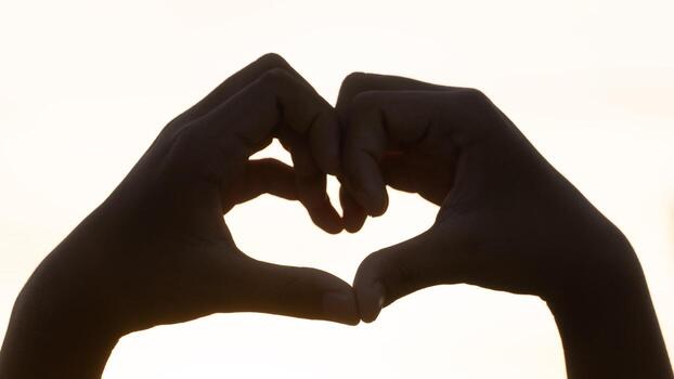 Hands creating a heart shape against a bright background, silhouetted by the light. This image evokes feelings of love romance and care. Perfect for Valentine's Day. photo