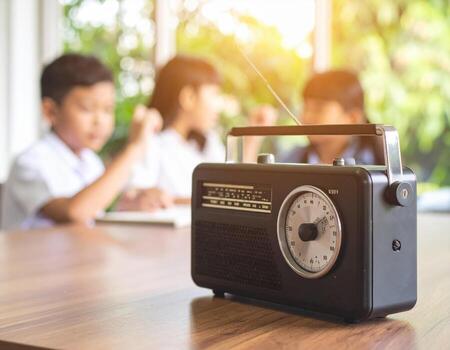 Vintage black radio on wooden desk with blurred children studying in background, creating nostalgic atmosphere of learning and connection photo