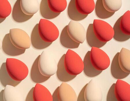 maquillaje esponjas arreglado en geométrico modelo en beige fondo, exhibiendo varios sombras de rojo y crema. vibrante colores crear visualmente atractivo y artístico monitor foto