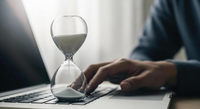 Hourglass on a laptop keyboard with a person typing, symbolizing time management photo