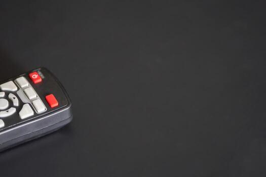 Close-up of remote control on black surface with red power button highlighted. photo