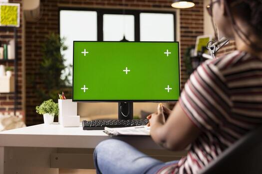 Black female entrepreneur analyzing business strategies at desk in home office. Focused remote manager using computer with blank chromakey screen template for work tasks and planning. photo