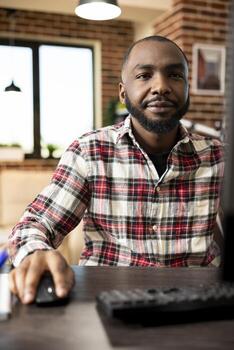 Portrait of remote male employee with intent expression, reading marketing research data on computer. African american businessman using desktop pc, focused on improving startup company financial year photo