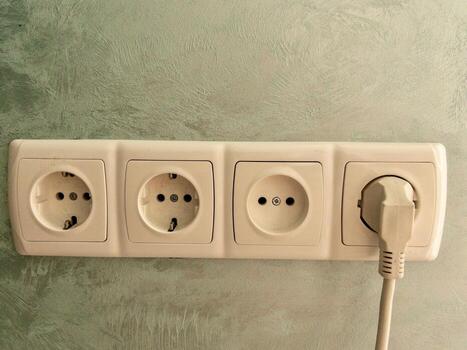 Triple electrical outlet with plug on textured wall. Close-up of a triple wall power socket, with one outlet in use photo