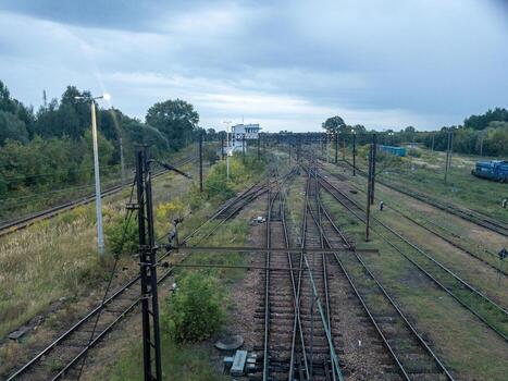 ferrocarril unión y traspuesta yarda con múltiple pistas, gastos generales de cadena y señales en verde paisaje debajo nublado cielo foto