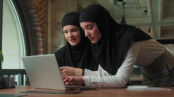 dois muçulmano o negócio mulheres dentro hijab meninas fêmea colegas de trabalho juntos usando computador portátil dentro escritório sorridente falando resolução conectados problema mulheres de negócios discutindo computador tecnologia estagiário menina com líder mulher video