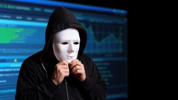 Anonymous hacker wearing a white mask and hoodie in front of computer screens photo