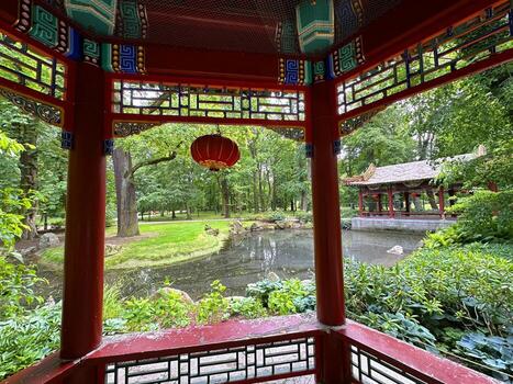 Tranquil Asian garden view from a traditional pavilion showcasing lush greenery, a serene pond, and a distant pagoda, creating a peaceful natural retreat atmosphere photo
