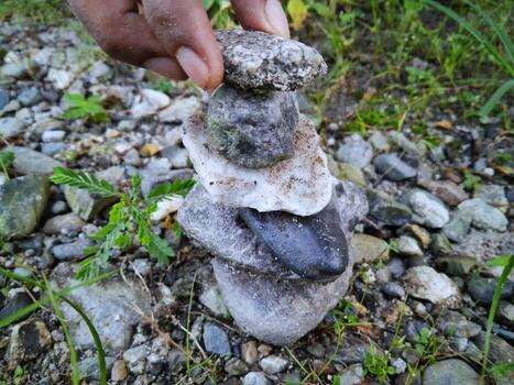 A hand is reaching for a stack of rocks, which are arranged in a pyramid shape. Concept of balance and harmony, as the rocks are stacked in a way that creates a visually pleasing and stable structure photo