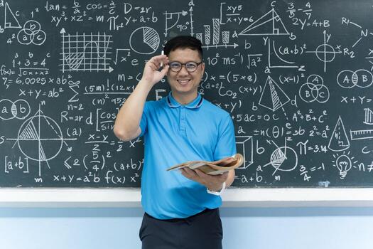Smiling mathematics teacher holding book in front of blackboard full of formulas and equations in class photo