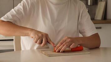 dentro uma acolhedor cozinha, uma mulher habilmente fatias uma vibrante cenoura em uma de madeira corte borda. a preparação vitrines dela culinária Habilidades e comprometimento para saudável comendo video