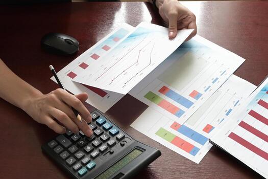 The image depicts someone analyzing financial data using a calculator and printed charts. photo