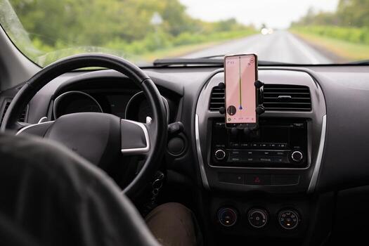 The photo shows a car dashboard with a smartphone displaying GPS navigation while driving.