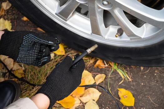 The image shows someone using an air compressor to add air to a car tire on the side of the road. photo