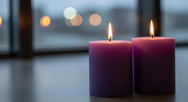 Two lit purple candles glow warmly in soft focus with bokeh lights behind them creating a serene atmosphere photo