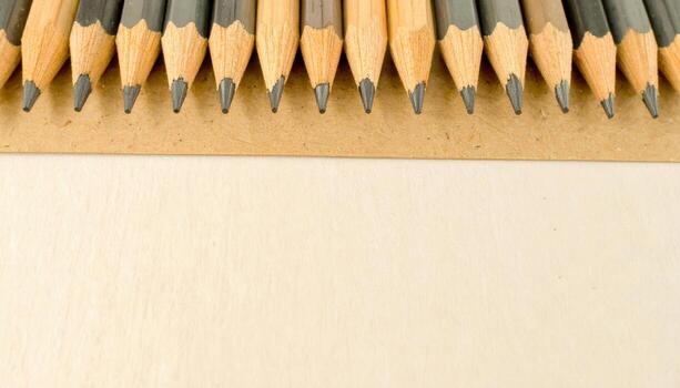 Close up sharpened graphite pencils aligned on kraft paper detail widescreen with wide copy space above stationery art supply design advertising background photo