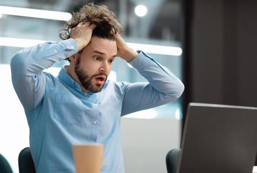 Oh No, Error Concept. Portrait of shocked scared man sitting at desk using pc, gasping with open mouth and grabbing his head. Stressed worried man suffering business problems reading bad negative news photo