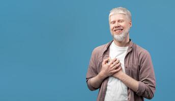 sincero albino chico participación manos en pecho, expresando gratitud y positivo emociones en turquesa estudio antecedentes. satisfecho hombre acuerdo palmas en corazón, sensación esperanza y amor foto
