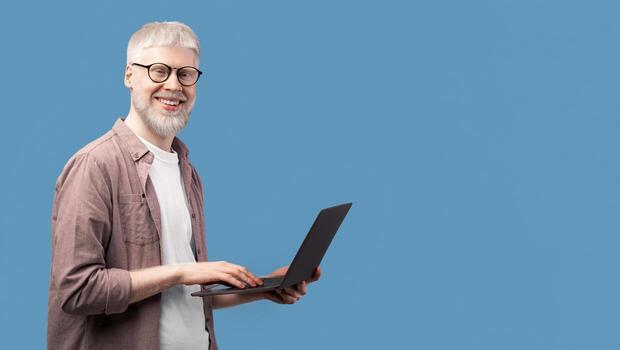 trabajando con alegría. joven albino hombre utilizando ordenador portátil y mirando con sonrisa a cámara terminado turquesa estudio antecedentes. barbado chico con raro apariencia posando con computadora foto