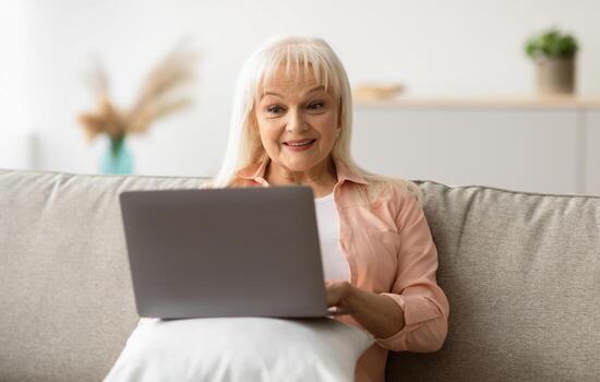 Technology And Resting Concept. Portrait of excited interested middle-aged woman using laptop, sitting on sofa with computer on lap, looking at screen and watching movie or reading news photo