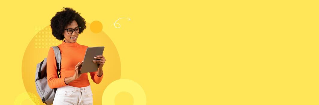 un estudiante con lentes y un mochila es enfocado en un tableta, disfrutando el proceso de aprendiendo. el brillante amarillo antecedentes mejora el moderno colegio atmósfera, enfatizando estudiar y compromiso. foto