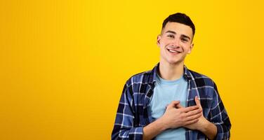 sincero joven chico poniendo manos en su corazón, expresando gratitud en naranja estudio antecedentes. de buen corazón milenario hombre acuerdo palmas en pecho, sensación amar, siendo romántico foto