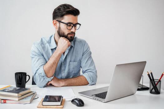 Young man working intently at his desk with laptop and books during daytime hours photo