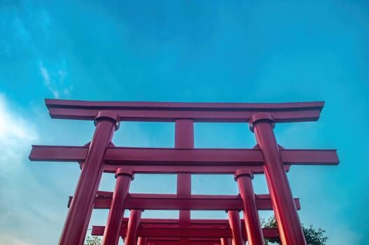 A low angle shot captures a series of vibrant red torii gates against a clear blue sky, creating a striking contrast and symbolizing a journey or transition in japanese culture. photo