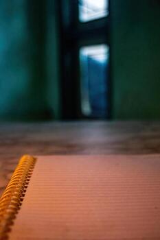 Close up on an open notebook with blank, lined pages, presenting a space for writing or sketching, set against a blurred backdrop of a room with an open doorway photo