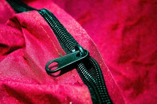 Close up on a red fabric bag with a black zipper. The zipper is partially open, revealing the texture of the material. The image highlights the details of the bag construction photo