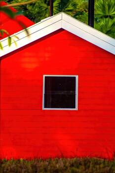 Exterior of a vibrant red house with a white trim and a square window, set against a backdrop of lush green foliage, creating a striking contrast and inviting atmosphere. photo