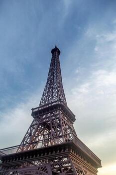 Eiffel tower against a blue sky with soft clouds, showcasing its intricate iron lattice structure and iconic silhouette, symbolizing travel and architectural achievement. photo