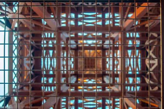 Abstract view of a tower structure through a metal grid, featuring geometric patterns and a sense of depth. The symmetrical design creates a visually intriguing composition. photo
