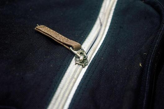 Close up on a sturdy black fabric with a white zipper and a brown leather pull tab. The zipper is partially open, revealing the texture of the fabric and the zipper metallic components photo