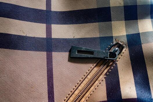 Close up on a beige and navy blue plaid fabric with a zipper. The zipper is partially open, revealing the stitching and texture of the material. The fabric has a classic pattern. photo