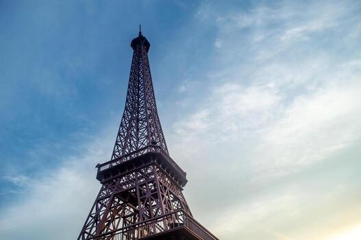 un bajo ángulo Disparo capturas el eiffel torre en contra un brillante cielo con suave nubes el torre intrincado herraje soportes afuera, simbolizando viajar, cultura, y arquitectónico logro. foto