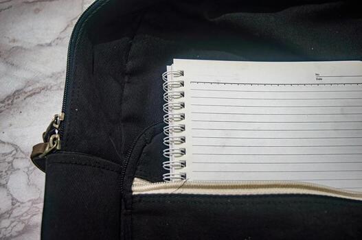 Close up shot of a black backpack with a white spiral notebook sticking out of a pocket, suggesting organization and preparedness for school, work, or travel, useful for education photo