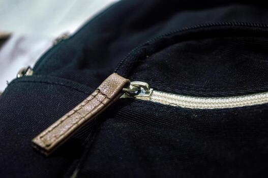 Close up on a black fabric bag featuring a silver zipper with a brown leather pull tab. The bag design highlights simplicity and functionality, ideal for everyday use and travel photo