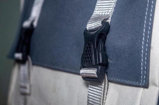 Close up shot of a gray and white backpack with a black plastic buckle and gray straps. The backpack is made of fabric with visible stitching and a textured surface photo