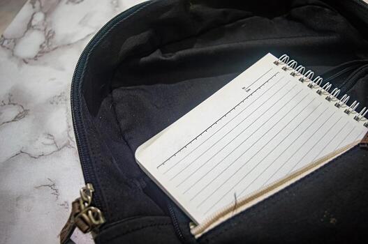Close up shot of a blank lined notebook inside a black bag. The notebook is open and ready for writing, suggesting concepts of organization, planning, or note taking for work or study photo