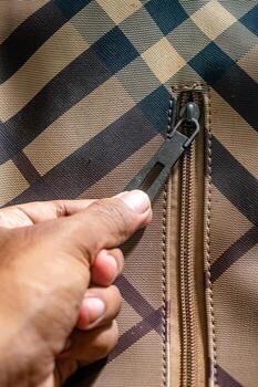 Close up on a hand pulling the zipper of a patterned fabric jacket. The jacket features a distinctive plaid design with intersecting lines and square shapes, creating a classic look. photo