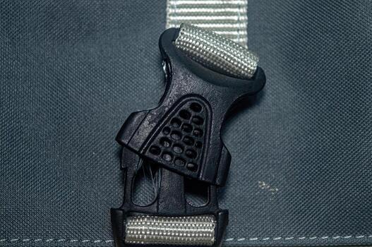 Close up of a black plastic buckle connecting a striped gray strap to a gray fabric bag, showcasing the fastening mechanism and material details in a functional design photo